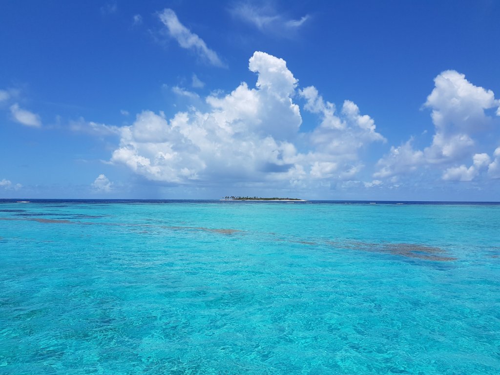 This photo shows a vast expanse of azure blue sea with low-lying islands in the distance