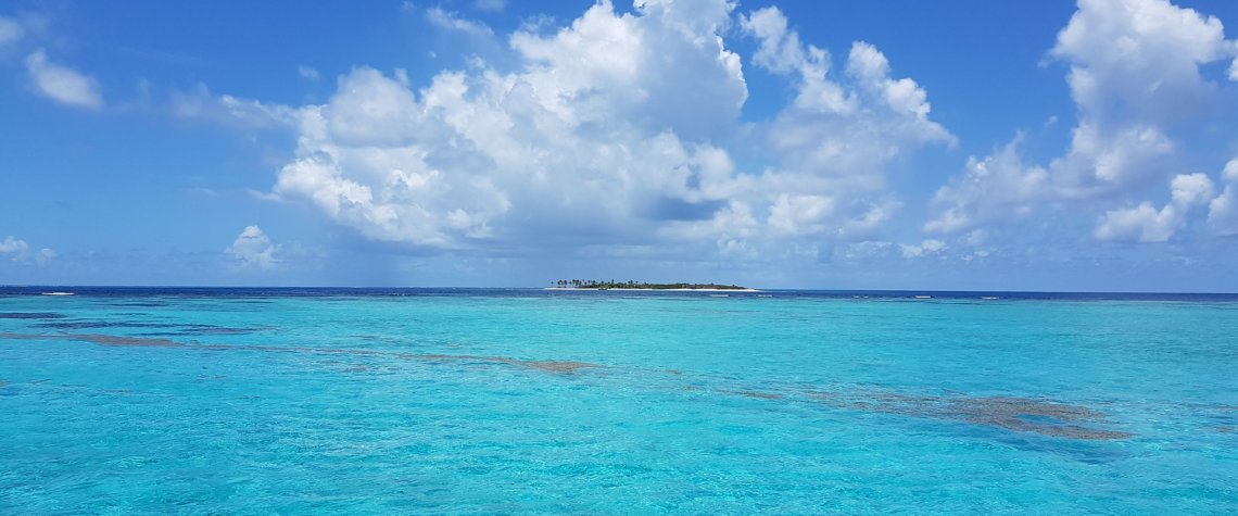 This photo shows a vast expanse of azure blue sea with low-lying islands in the distance
