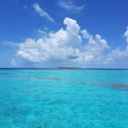 This photo shows a vast expanse of azure blue sea with low-lying islands in the distance