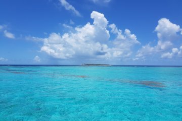 This photo shows a vast expanse of azure blue sea with low-lying islands in the distance