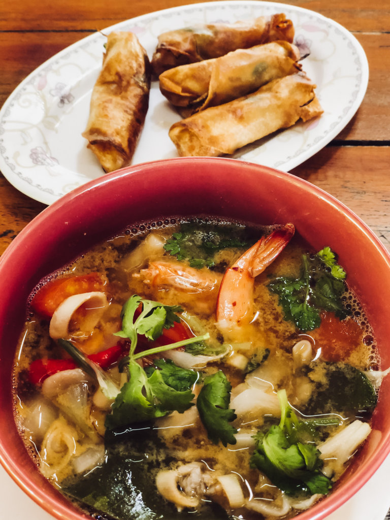 This photo shows a bowl of delicious tom yam and a plate of spring rolls