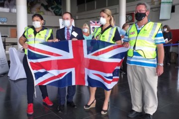 This photo shows the High Commission team wearing masks and hi-viz jackets and holding the Union Flag