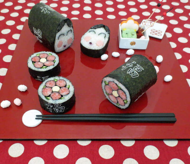 This photo shows a red square tray with decorative pieces of sushi, some with faces running through them