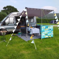 This photo shows our blue-grey campervan with its sun canopy out decorated with blue and yellow bunting