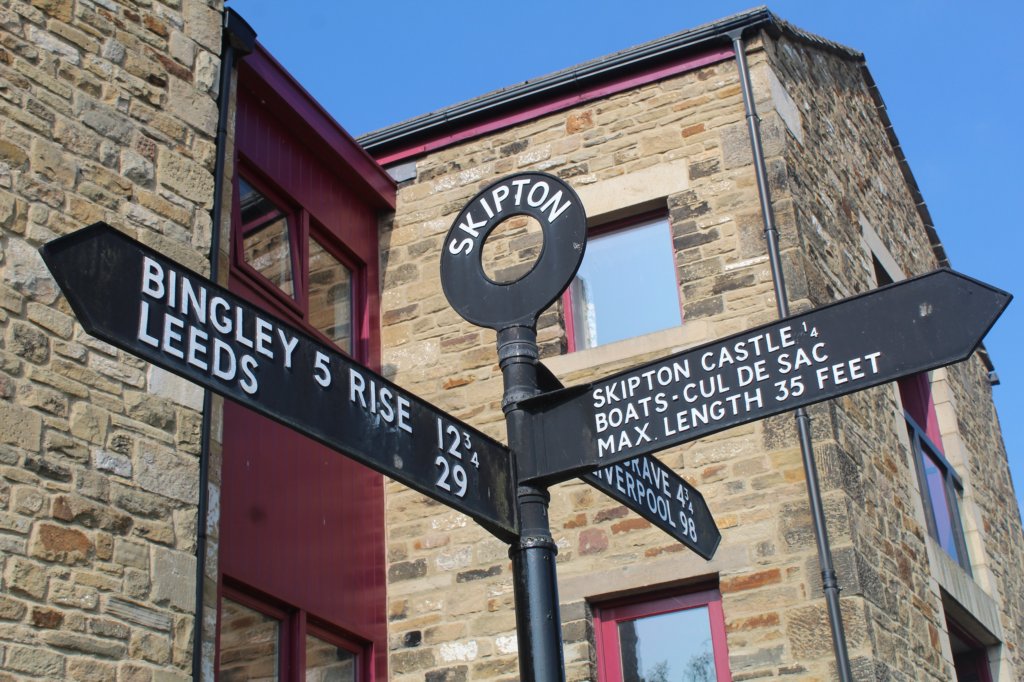 This photo shows a black signpost with distances to Leeds and Liverpool as well as more local sites