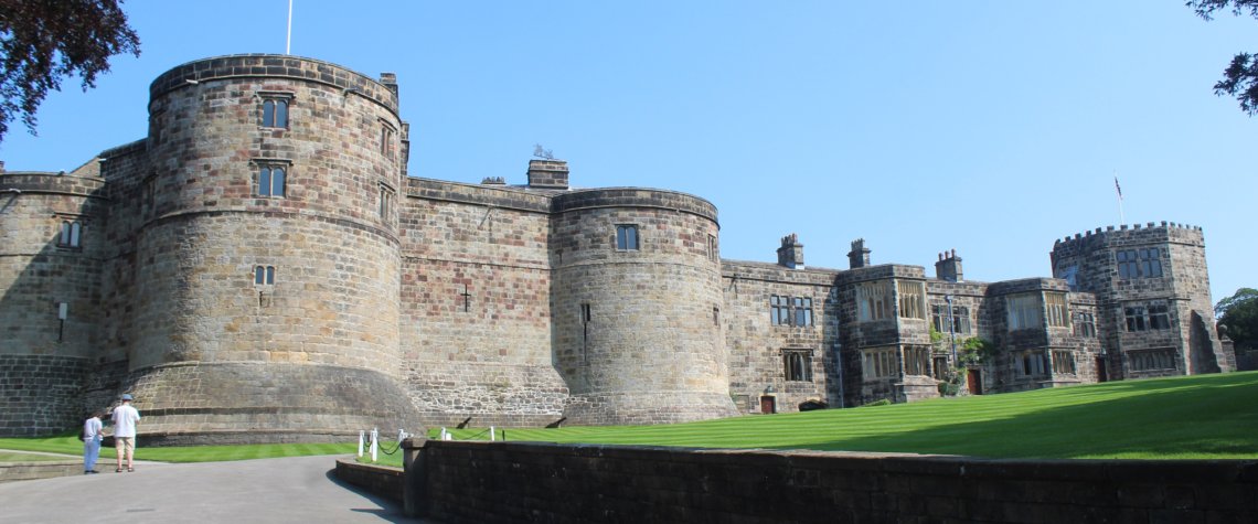 This photo shows the imressive main part of Skipton Castle with lush green lawns in the foreground