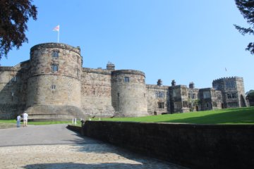 This photo shows the imressive main part of Skipton Castle with lush green lawns in the foreground