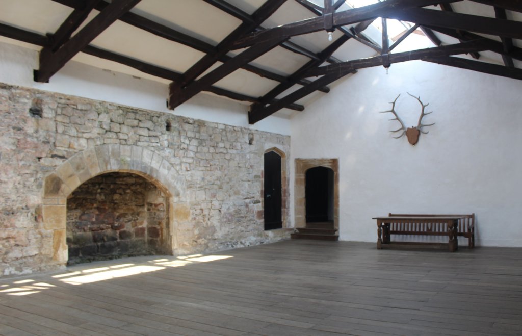 This photo shows the banqueting hall of Skipton Castle with its oak-beamed ceiling and large stone fireplace