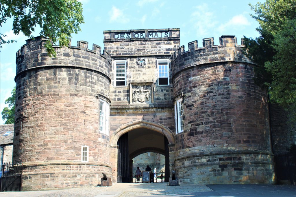 This photo shows the gatehouse of Skipton Castle with two substantial round stone towers topped with the word, 'desormais'.