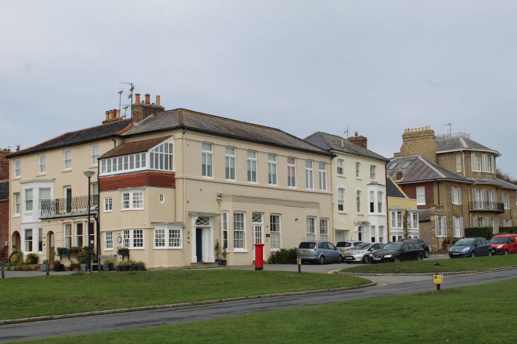This photo shows a large white Georgian building with a brilliant red post box in the foreground