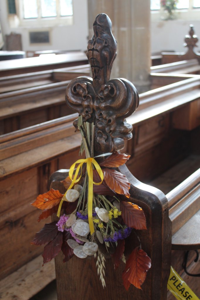 This photo shows the end of a pew with ornate carving and decorated with flowers
