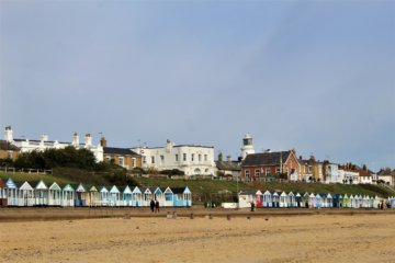 This photo shows an expanse of sandy beach with beach huts in the distance