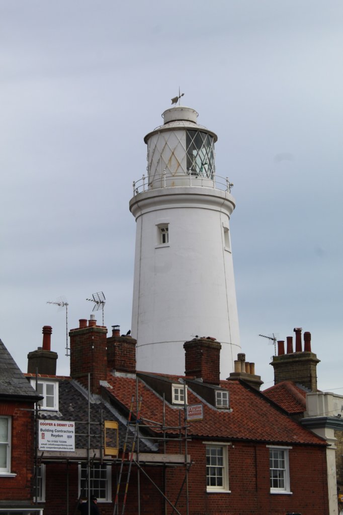 This photo shows the majestic white Southwold lighthouse with red tiled roofs of houses in the foreground