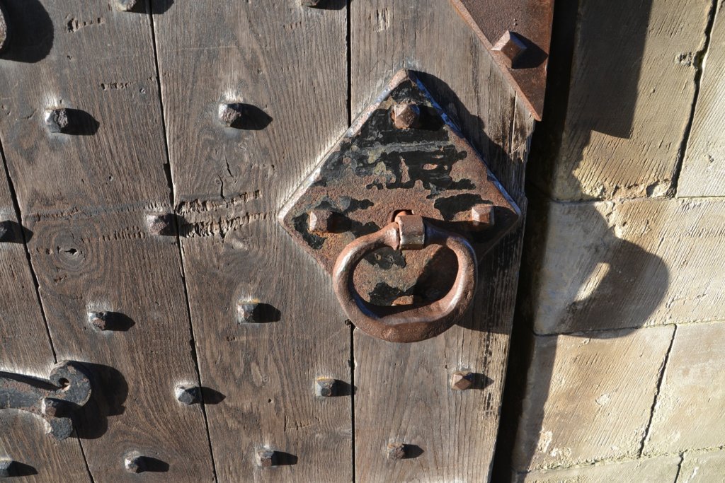 This photo shows part of an old oak door with metal rivets and a round door handle