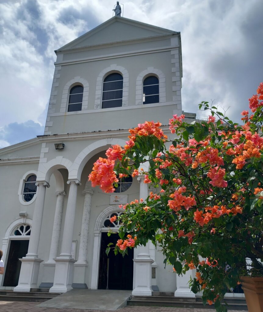 This photo shows the front of the cathedral with a beautifully bush covered in orange blooms in the foreground.