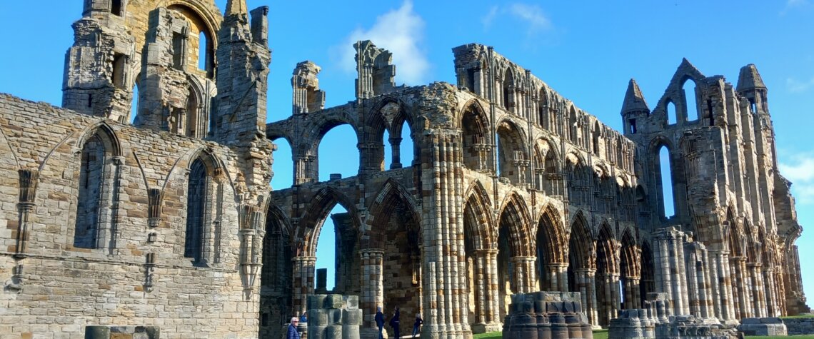 This photo shows a wide view of Whitby Abbey ruins set against an azure blue sky