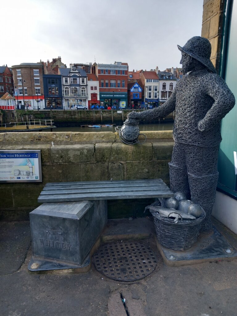 This photo shows a sculpture of a fisherman looking over a wall towards the estuary of the River Esk 