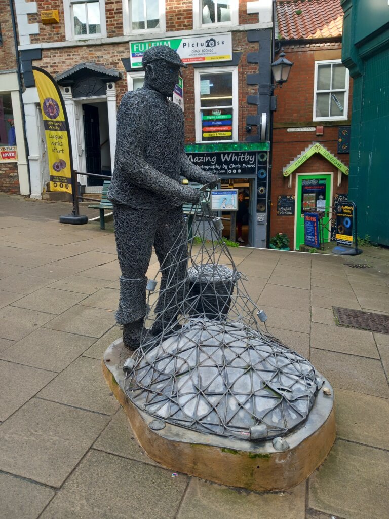 This image shows a sculpture of a fisherman mending his nets as part of Whitby's Walk with Heritage Trail