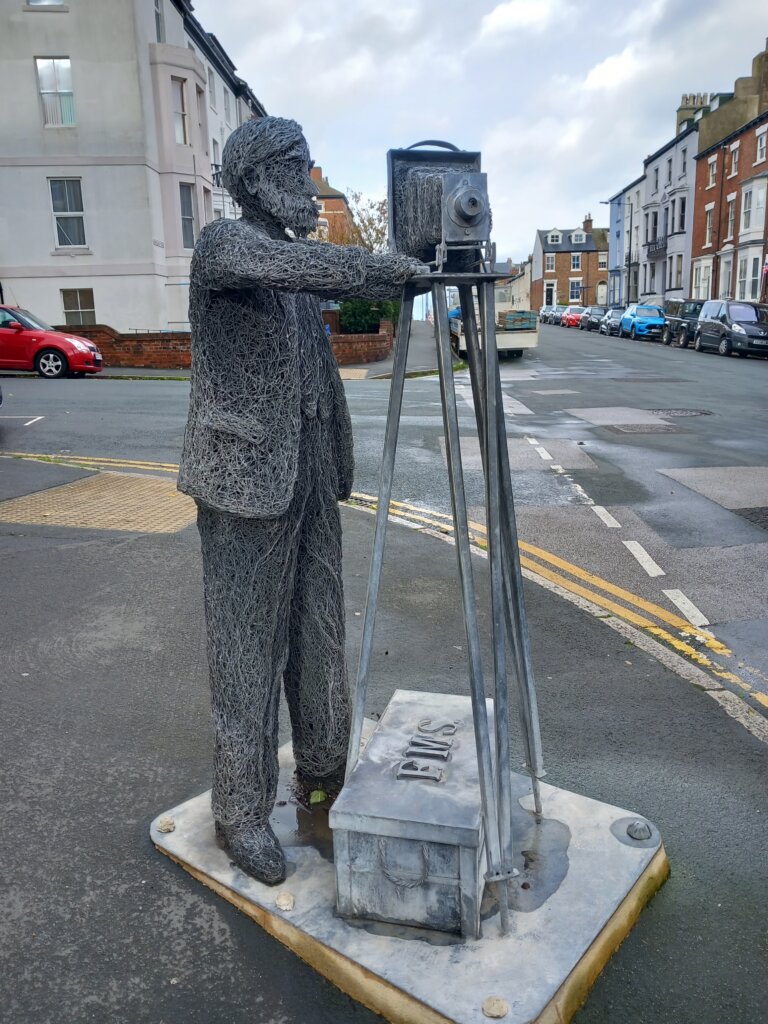 This image is of a sculpure of a photographer with an old fashioned camera on a tripod