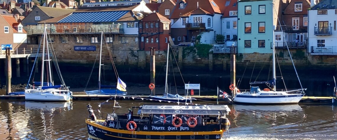 This photo shows a tourist boat leaving Whitby harbour with East Cliff and St Mary's Church in the background
