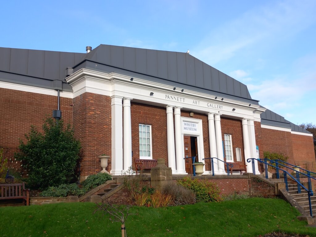 This photo shows the front of the building that houses Whitby Museum and Art Gallery. It is red-brick built with white columns at the front.