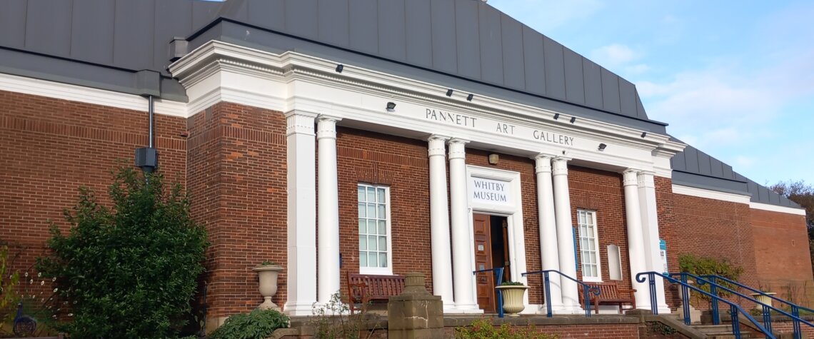 This photo shows the front of the building that houses Whitby Museum and Art Gallery. It is red-brick built with white columns at the front.