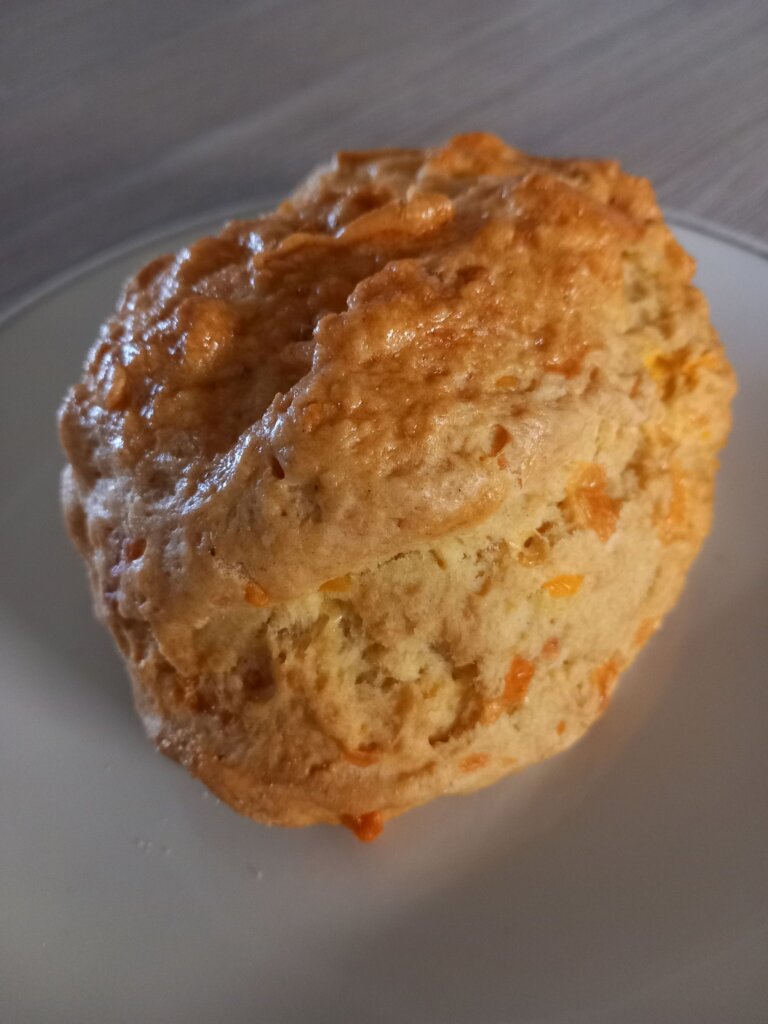 This photo shows a large golden brown scone with flecks of grated orange cheese clearly visible