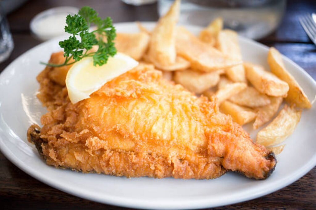 This photo shows traditional fish and chips on a white oval plate garnished with parsley and a lemon wedge