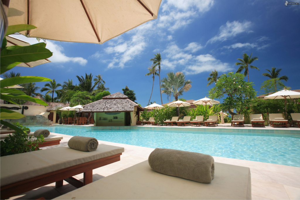 This photo shows sun loungers arranged around a pool.  The sun is shining and the sky is blue.