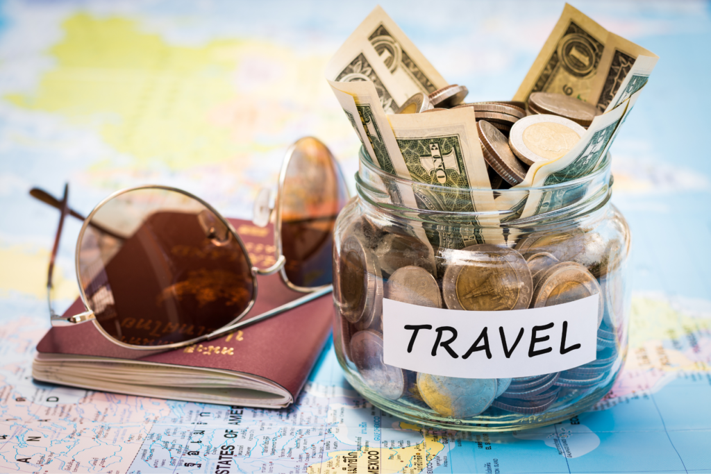 This photo shows a jar stuffed with cash sitting on top of a world map with a passport and sunglasses next to it.
