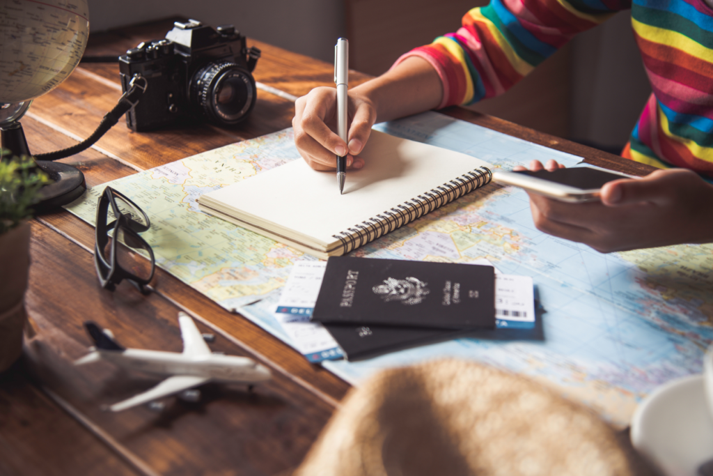 This photo shows someone making notes surrounded by a world map, passports, and a camera